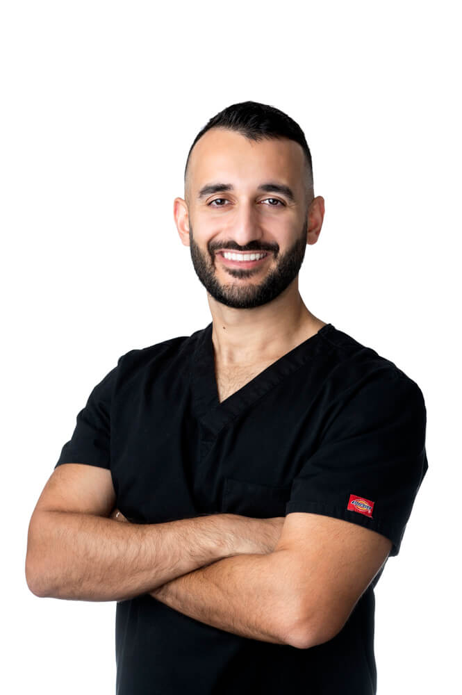 Dr. Paradis Esi of ESI Dentistry - Esthetic Smiles & Implants standing with arms crossed and smiling in front of white background