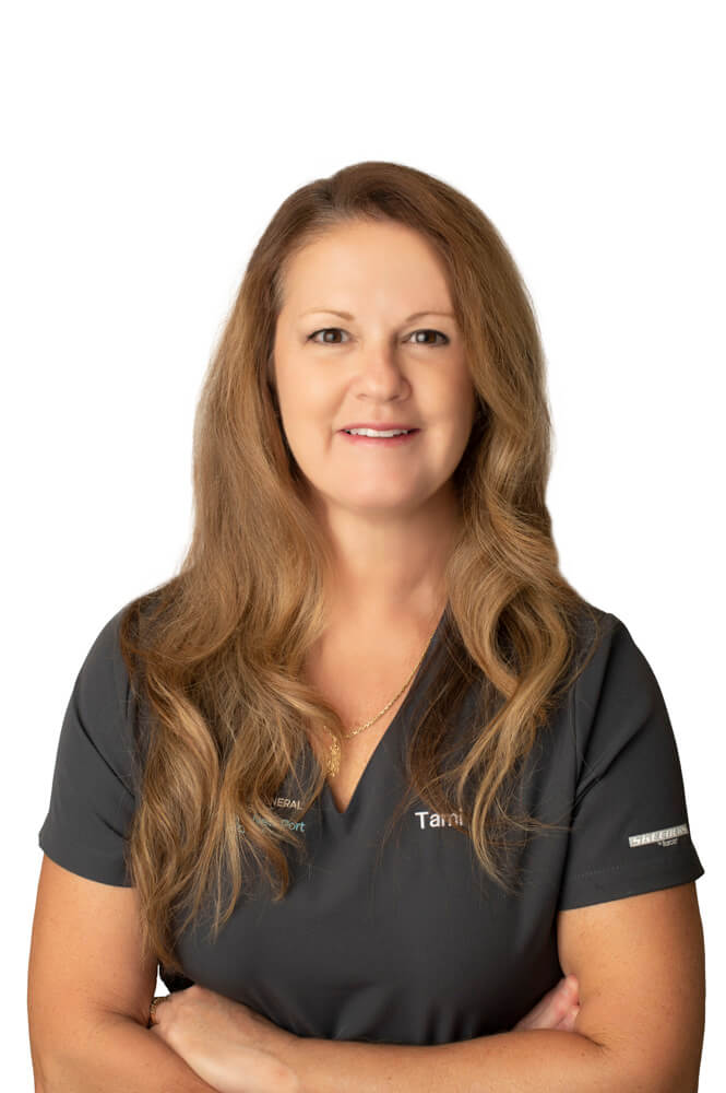team member Tami Schifflin of ESI Dentistry - Esthetic Smiles & Implants standing with arms crossed and smiling in front of white background